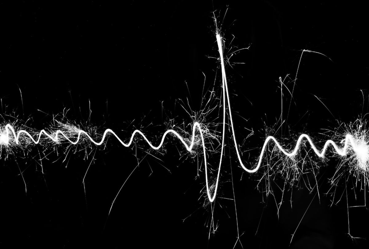 A white electric sine-wave against a black background, it looks like a pulse