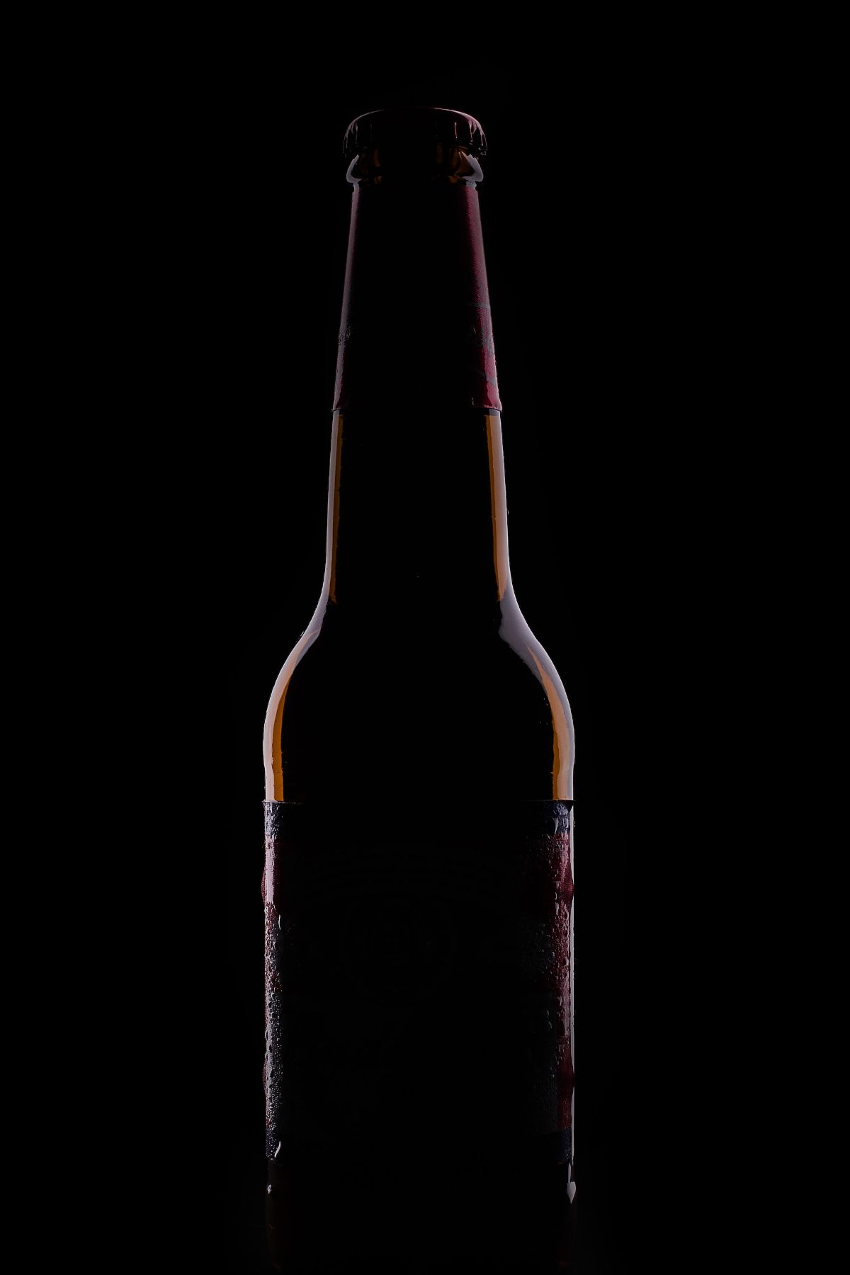 A dimly lit brown beer bottle without no label against a black background.