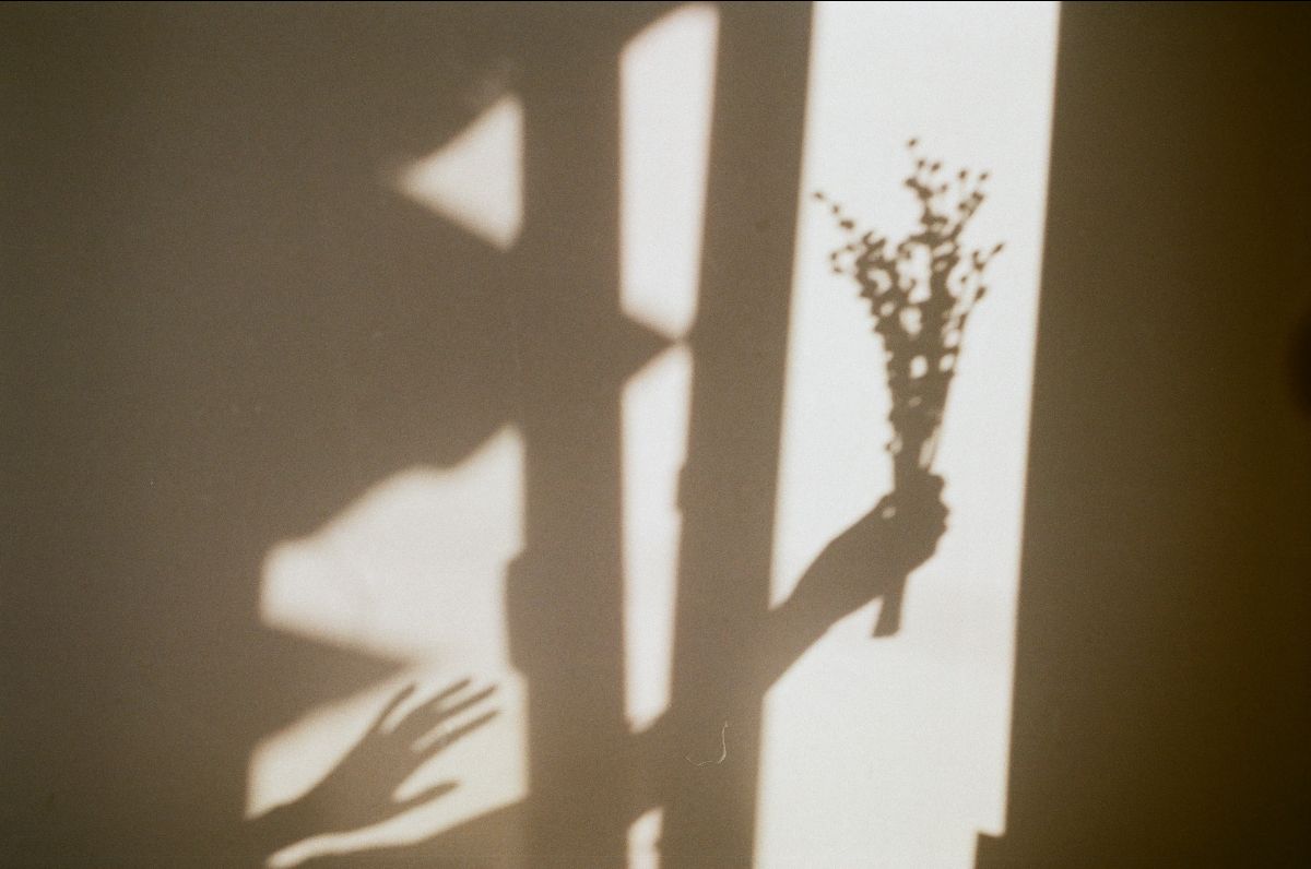 Gray shadow of a hand holding dainty flowers against a beige wall
