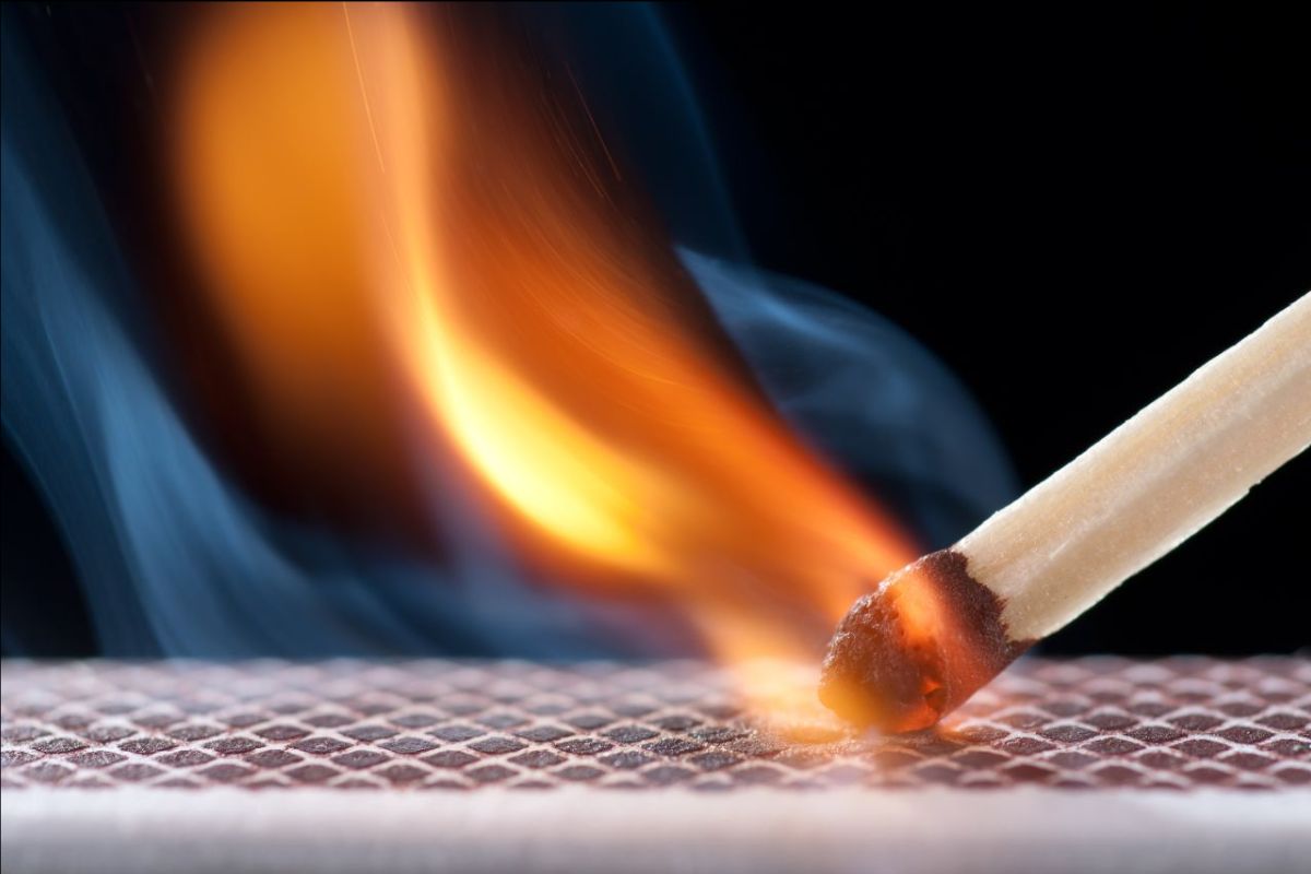 A close up of a match and it's flame as it's being lit on a matchbook