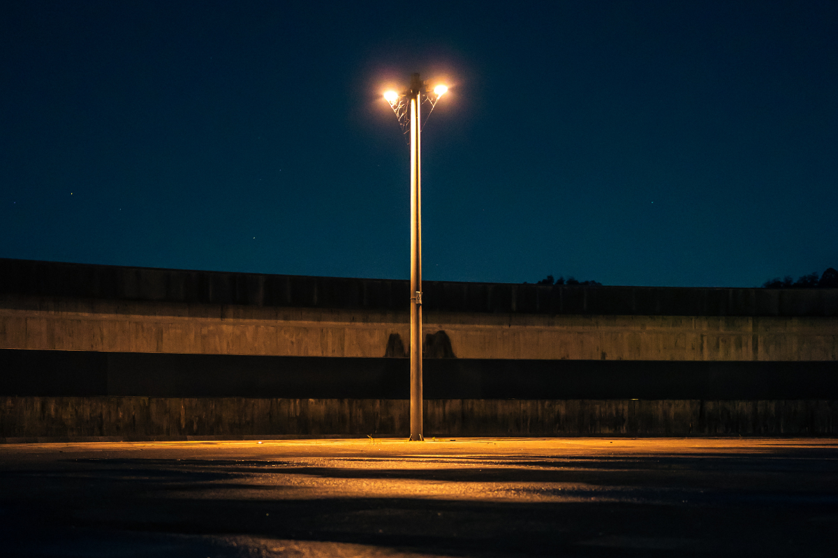 A city street lamp with two yellow lights lighting up an empty street with with a dark blue night in the background