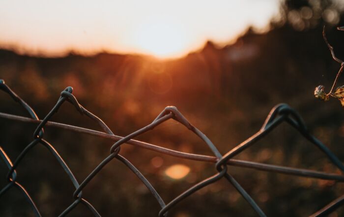 a metal fence with a sunset behind it
